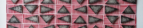 Black and white triangles in a horizontal grid, floating over a layer of red and white striped rectangles. Rotating Triangles (Black on Red) by Bill Brookover